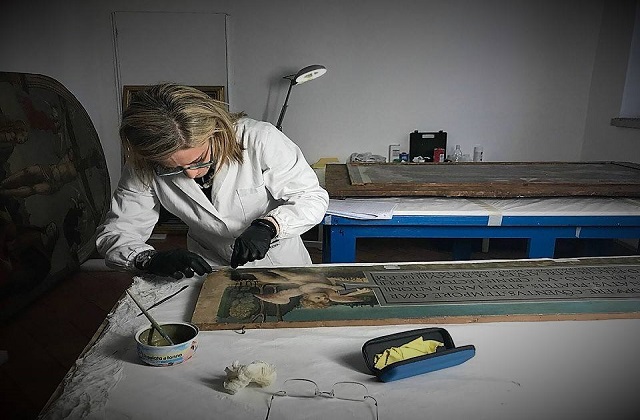 Una restauratrice all'opera su una tela salvata dal sisma